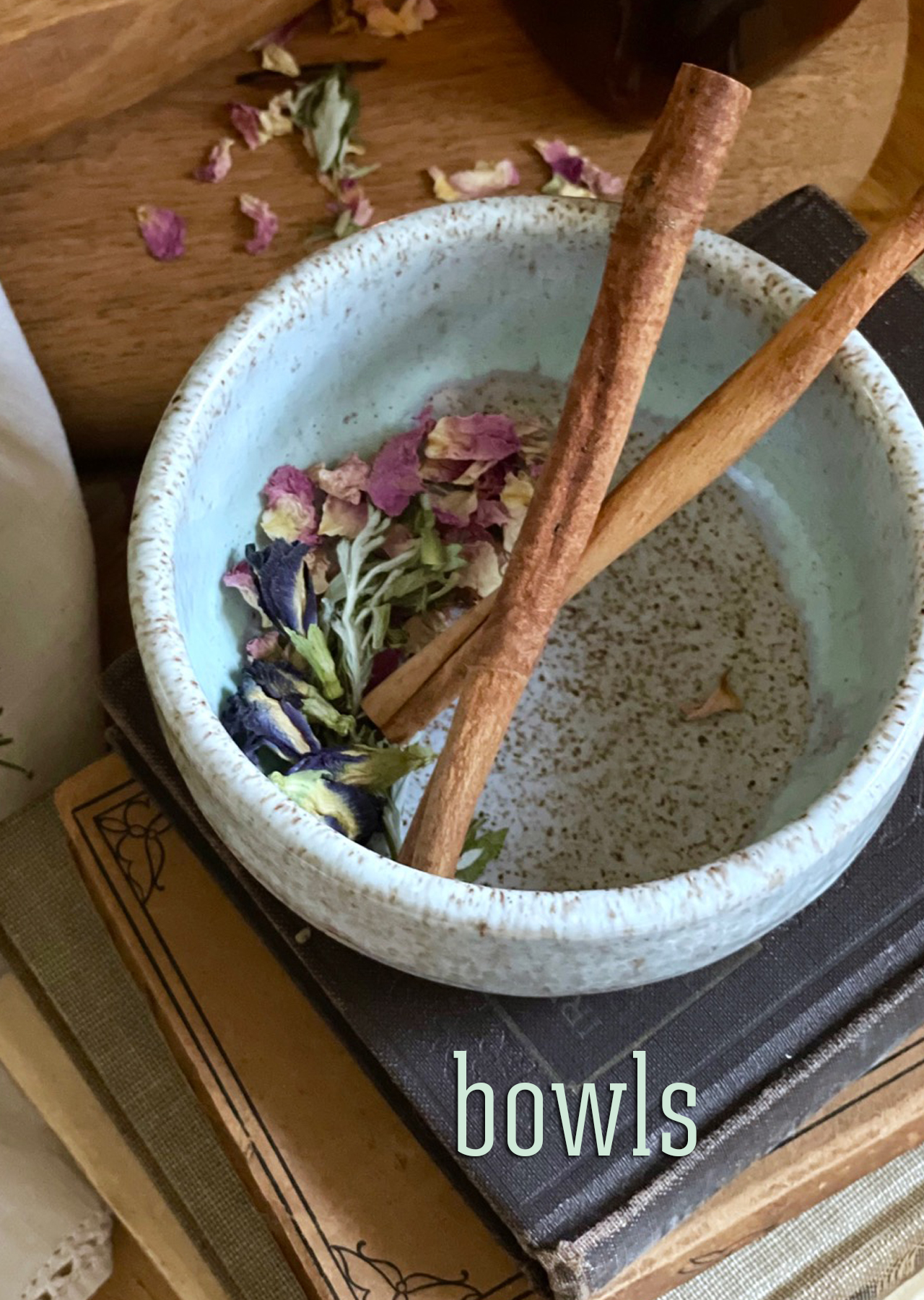 Icy blue bowl with the speckles of the clay coming through the glaze, styles on old books with cinnamon sticks and dried rose petals and mugwort