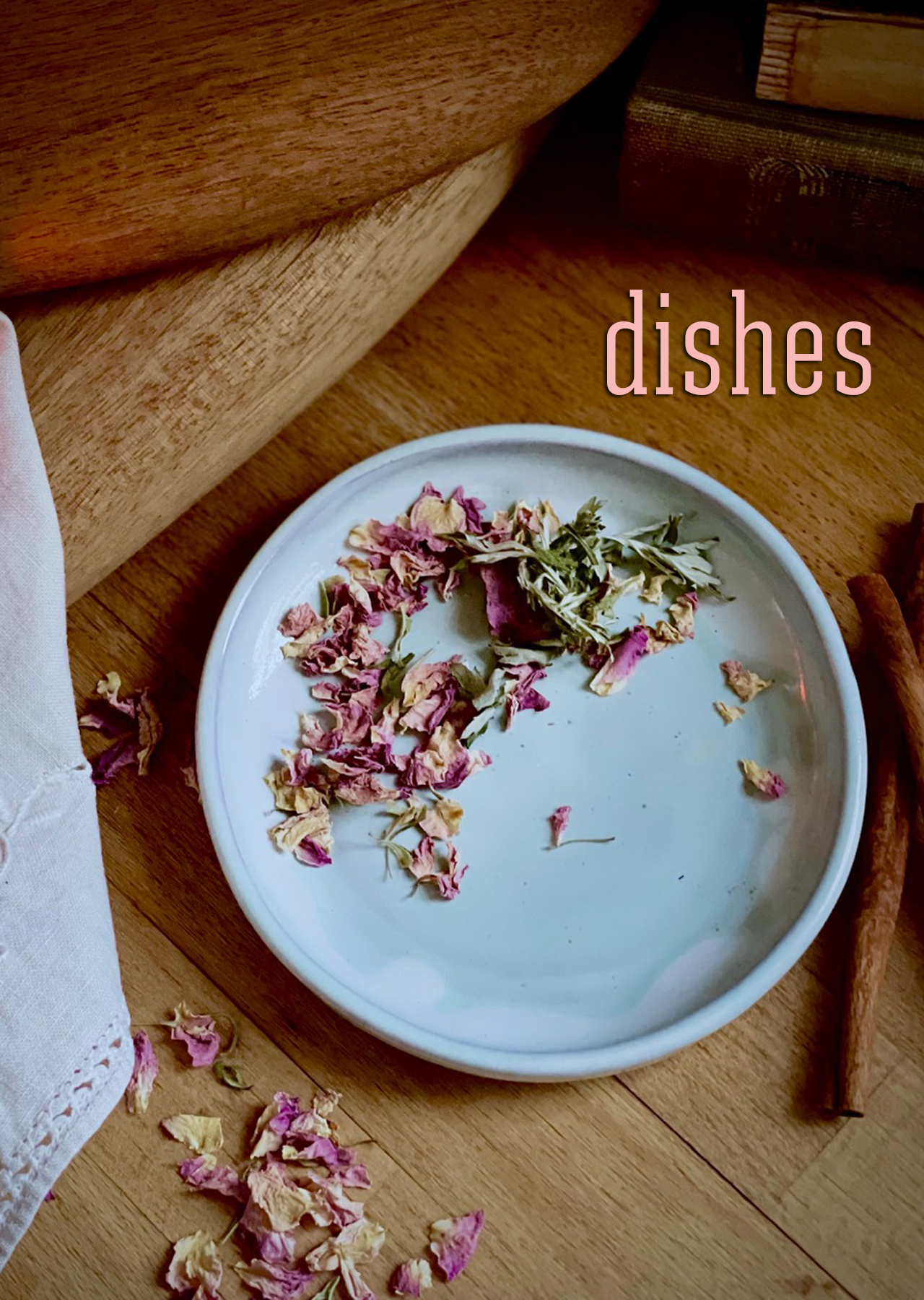 Icy blue glazed dish shown on a warm wood surface styled with dried rose petals, cinnamon sticks, and dried mugwort